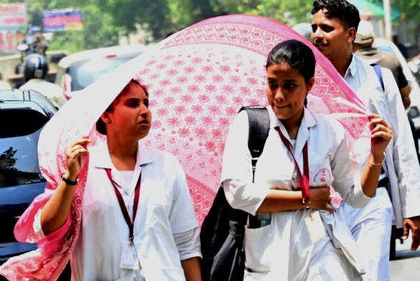 कानपुर में तेज धूप से बचने के लिए अंगौछे से सिर ढक कर निकलते हुए युवतियां का छायाचित्र