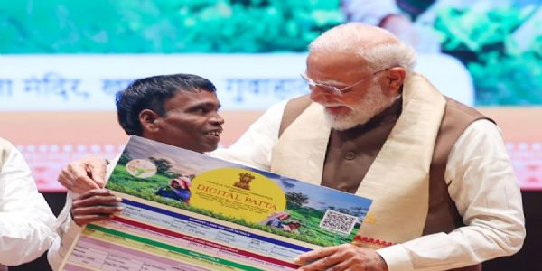 गुवाहाटीः गुवाहाटी में शुक्रवार को आयोजित कार्यक्रम में चाय जनजाति समुदाय के एक व्यक्ति को भूमि का पट्टा प्रदान करते प्रधानमंत्री नरेन्द्र मोदी